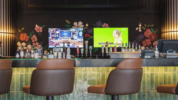 A bar area with stools, a counter with bottles, and a television screen displaying a woman. - Hilton Niagara Falls/Fallsview Hotel & Suites (Niagara Falls)