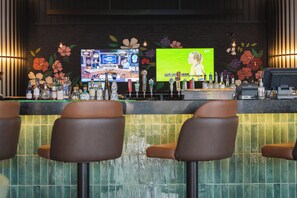 A bar area with stools, a counter with bottles, and a television screen displaying a woman.