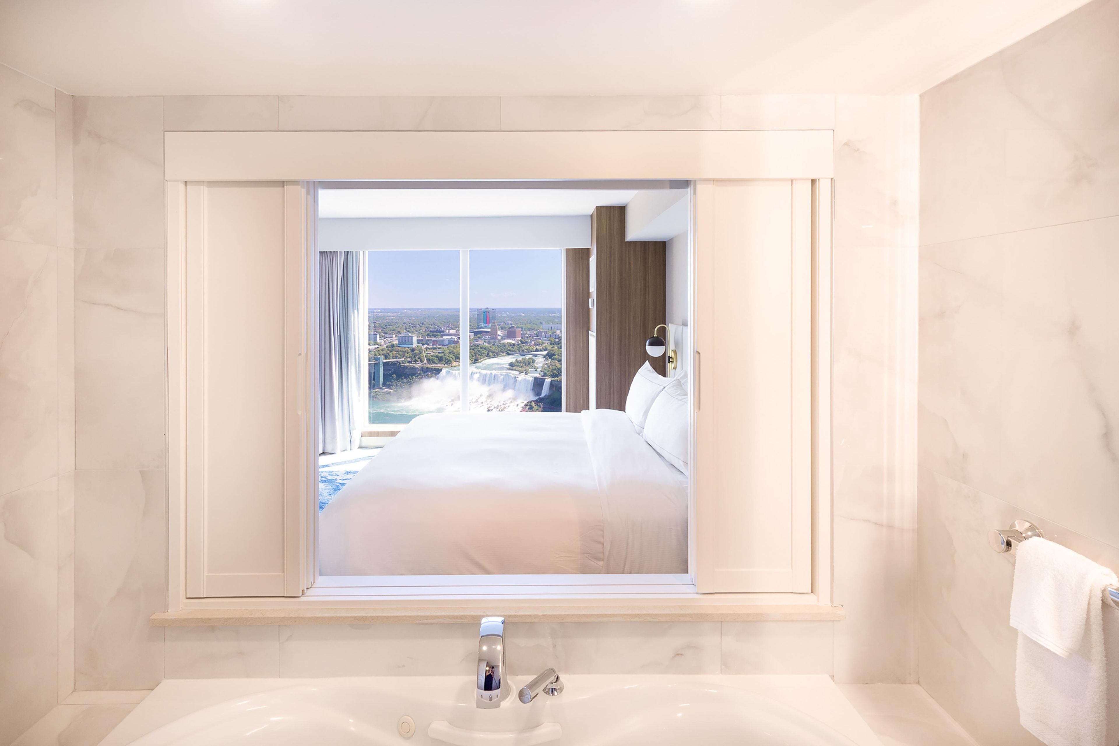 Habitación de hotel con una cama grande, un baño con bañera y una ventana con vista a la ciudad.