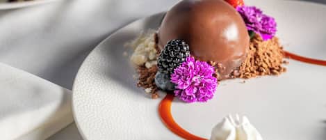 A dessert plate with a chocolate sphere, berries, and decorative flowers.
