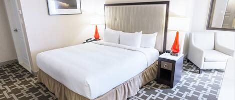 A hotel room with a large bed, bedside tables, a chair, a nightstand with a lamp, and a framed picture on the wall.