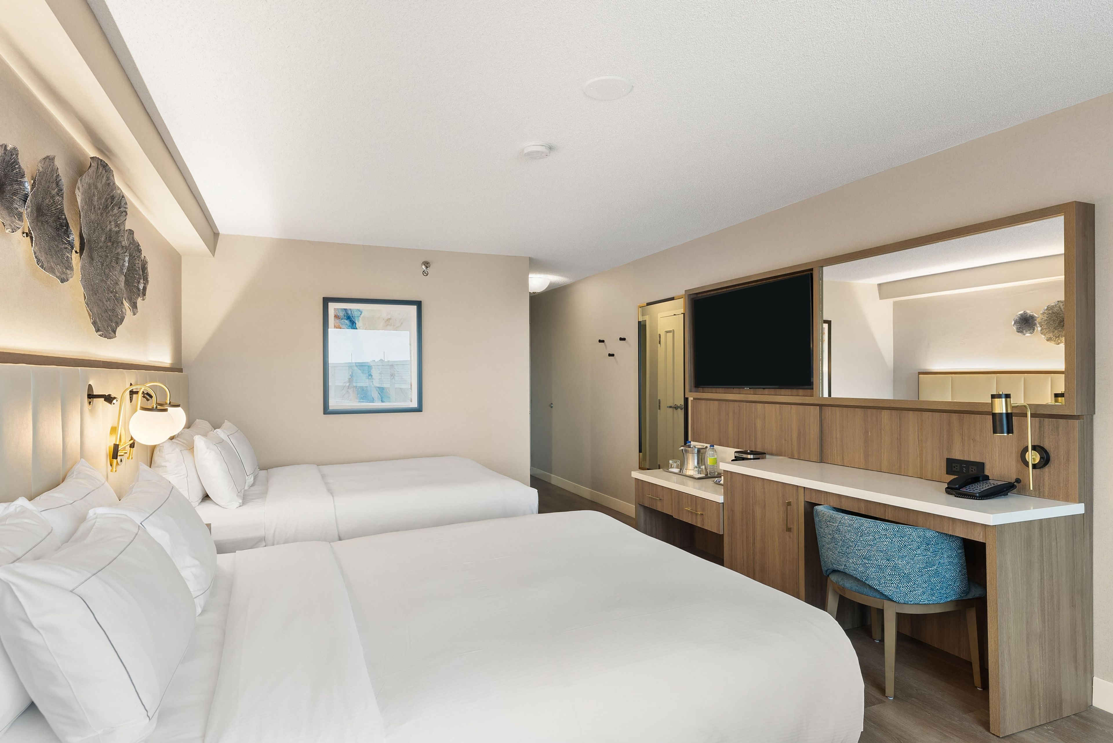 Habitación de hotel con cama, mesita de noche, escritorio, silla y un espejo grande.