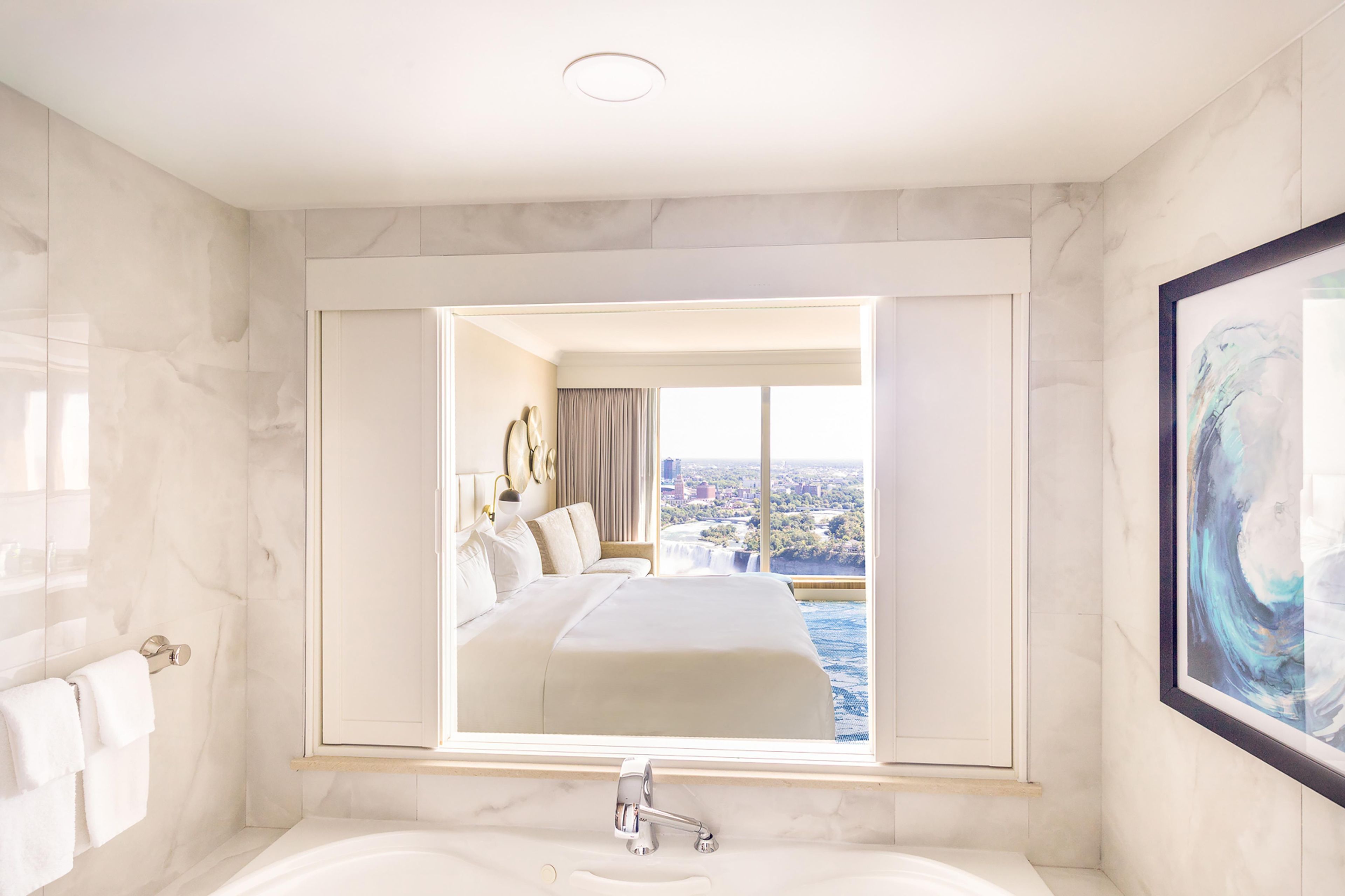 Quarto de hotel com um espelho grande refletindo uma cama e a vista da cidade.
