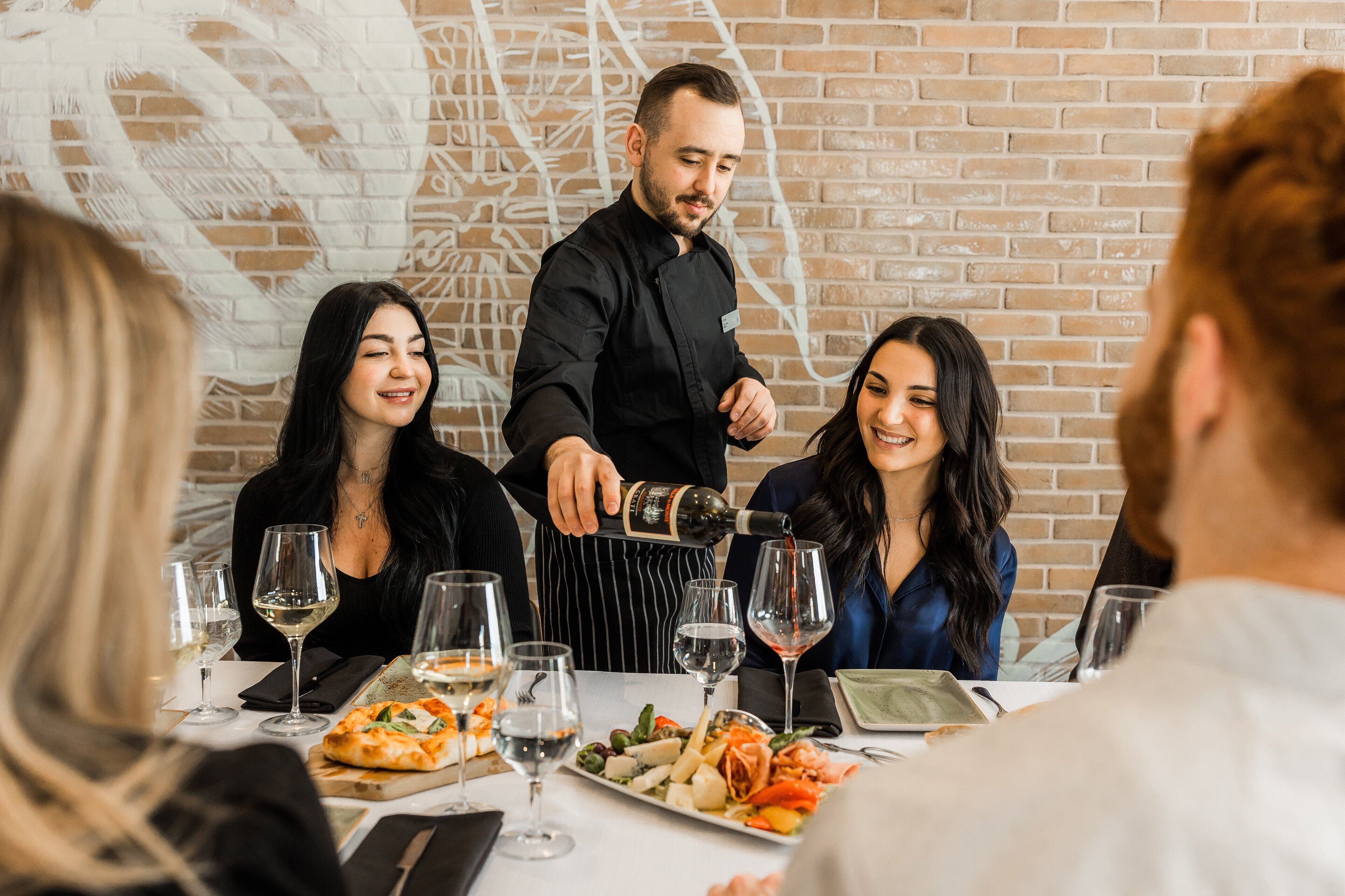 A restaurant setting with a brick wall, a pizza on the table, and wine glasses.