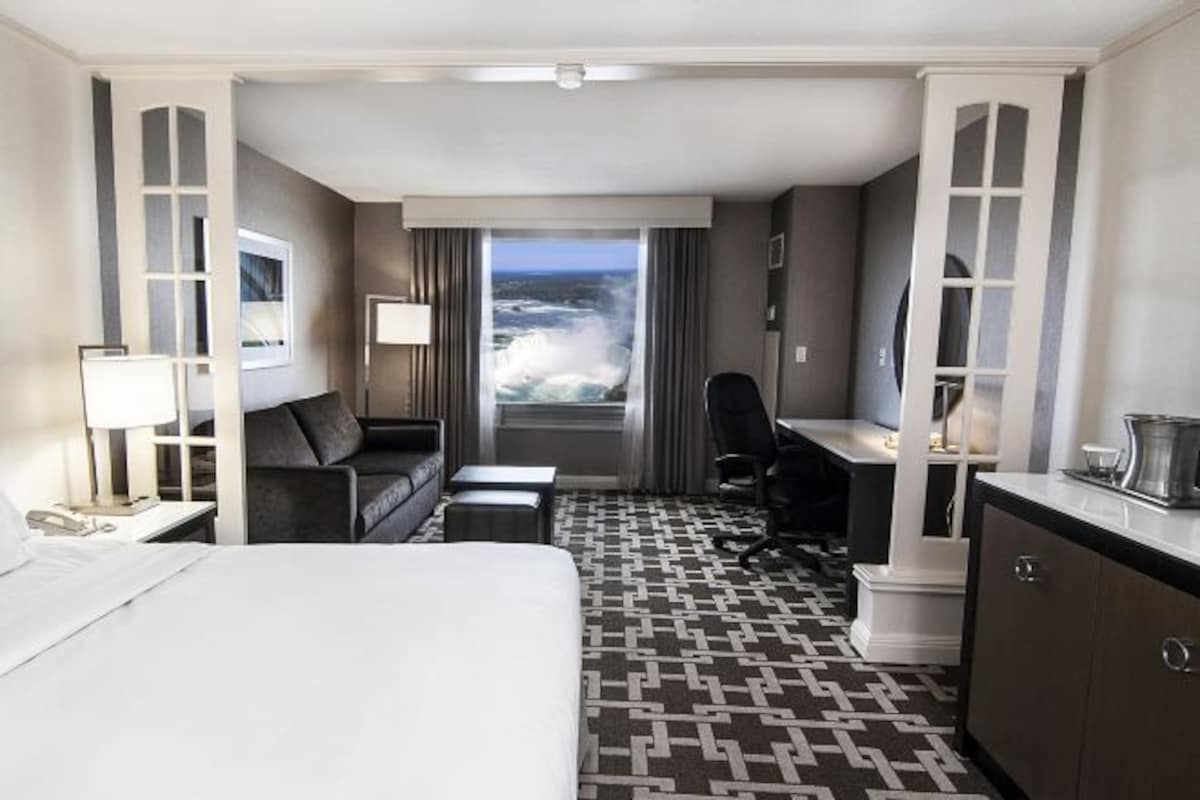 Ett hotellrum med en säng, ett skrivbord, en stol, en soffa och utsikt över havet.
