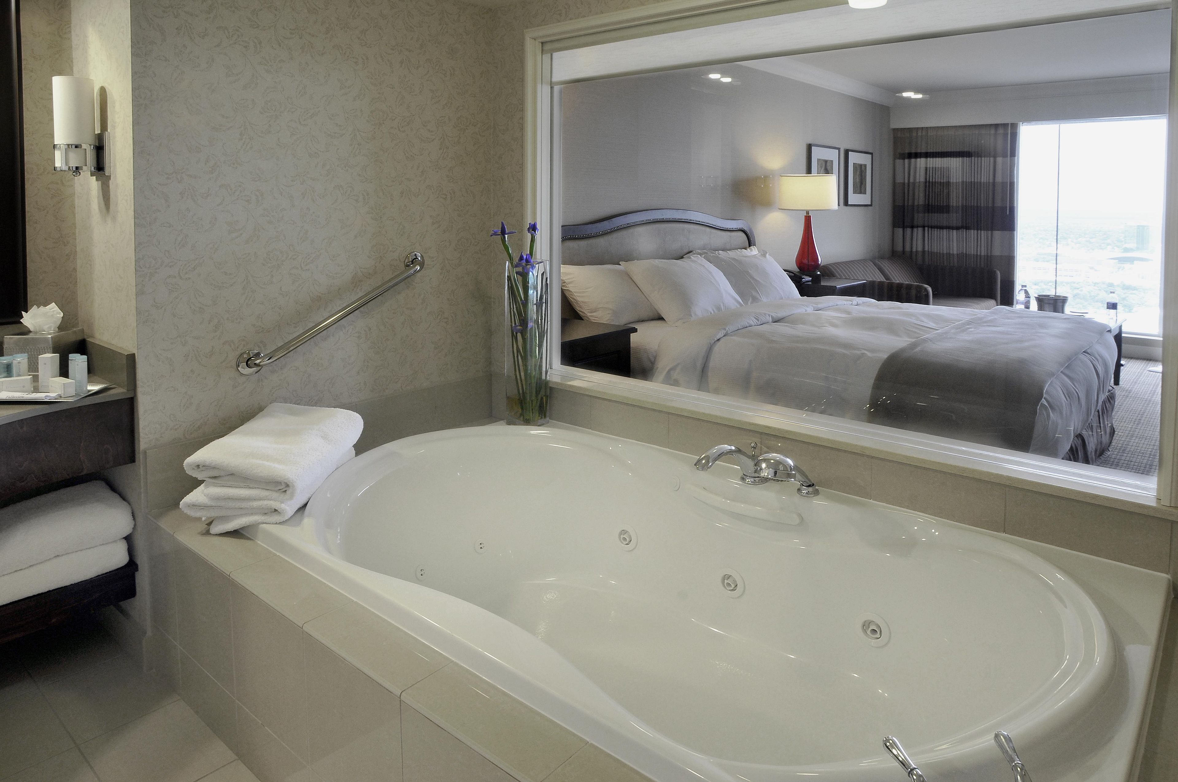 A hotel bathroom with a large bathtub, a mirror reflecting the room, and a handrail.