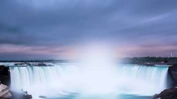 A waterfall with a misty spray, surrounded by rocky terrain and a distant city skyline.