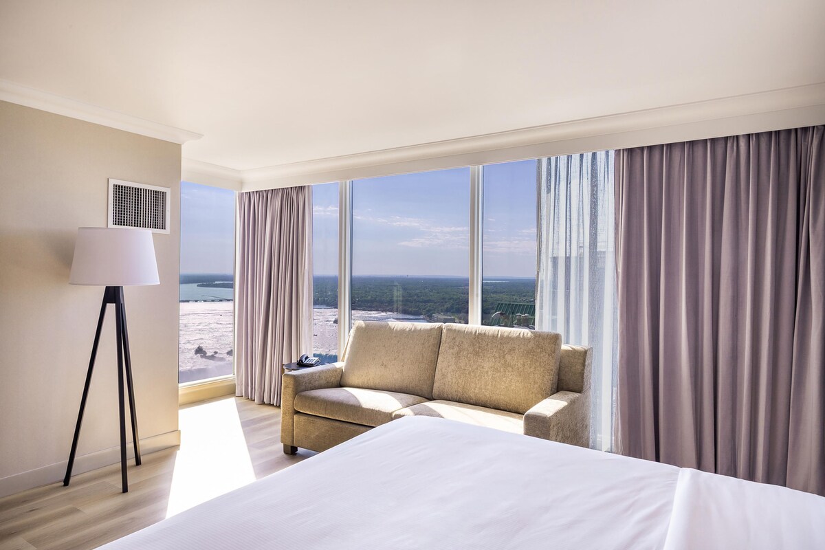 A hotel room with a bed, a sofa, a lamp, and a view of the ocean.