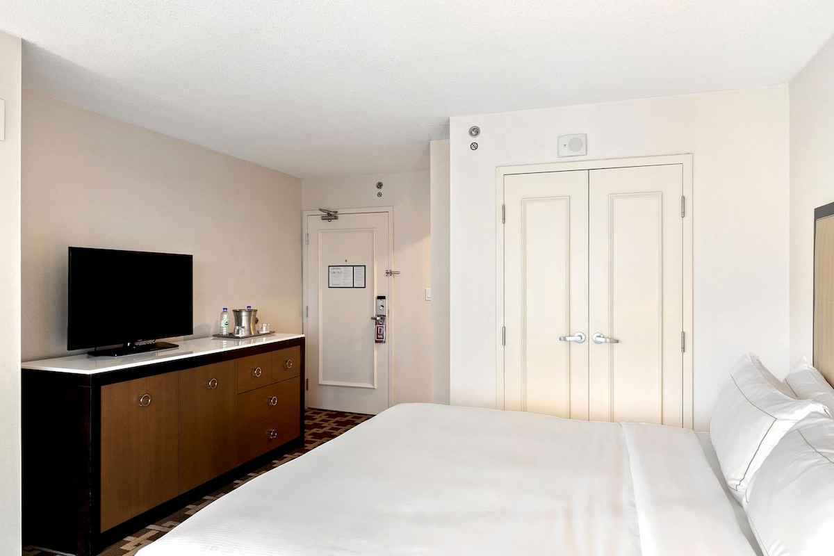 A hotel room with a bed, a television on a dresser, a minibar, and a door with a lock.