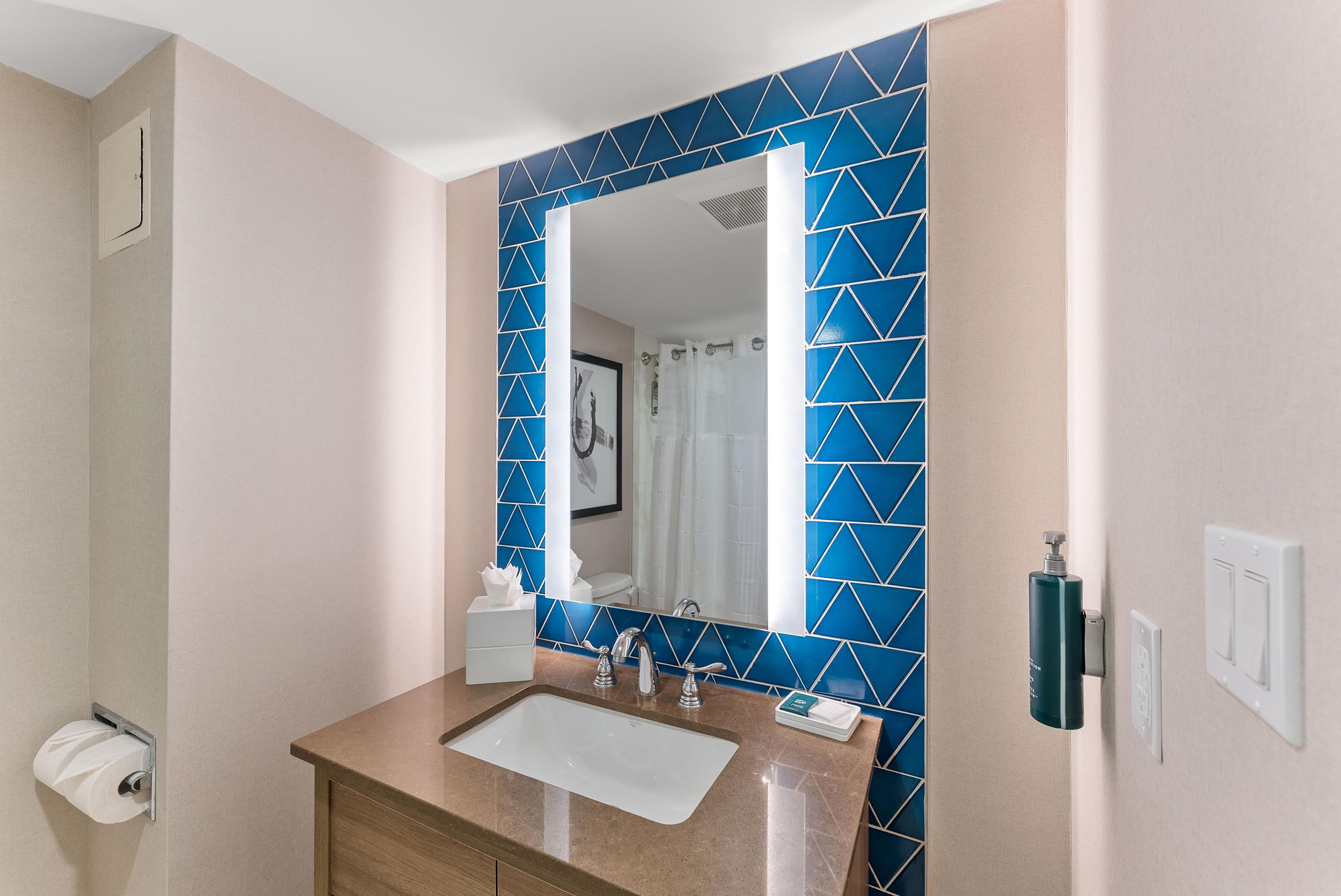 Un baño con lavamanos, espejo y salpicadero de azulejos con diseño geométrico azul.