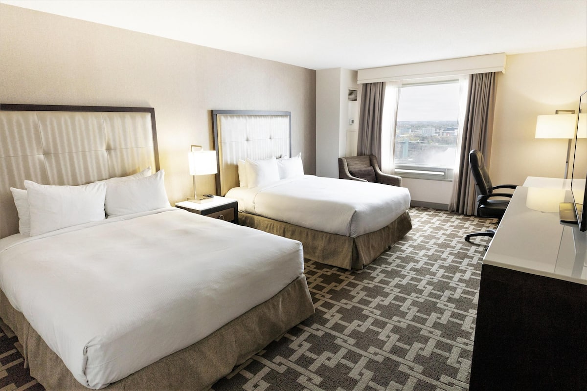 Une chambre d’hôtel avec deux lits, un bureau, une chaise, une fenêtre donnant sur un paysage agréable et une moquette à motifs.