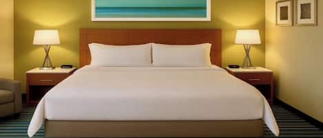 A hotel room with a large bed, two bedside tables with lamps, a headboard, a painting on the wall, and a striped carpet.