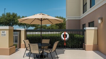 Un patio al aire libre con una mesa, sillas, un paraguas grande y un flotador colgado de una puerta.