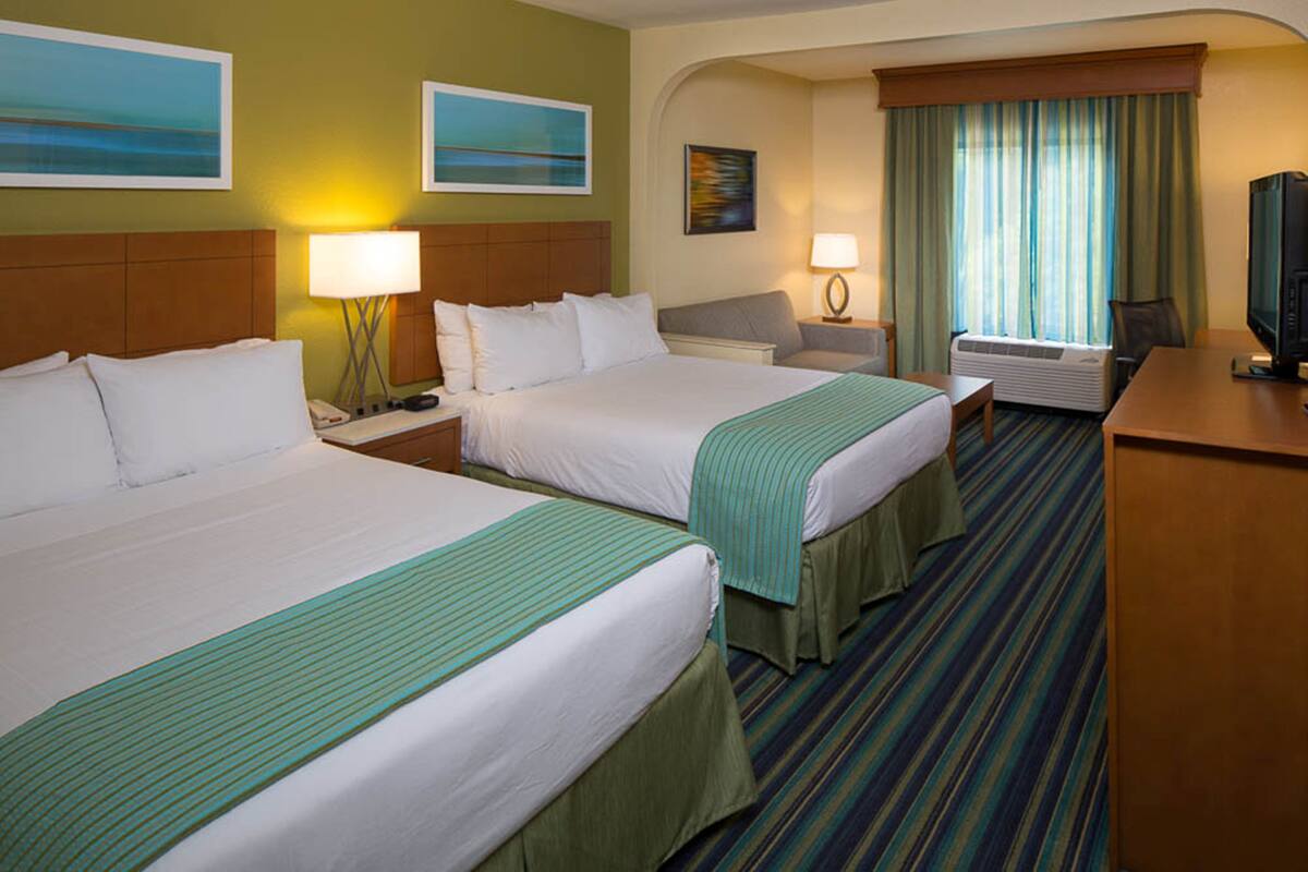 A hotel room with two beds, a desk, a television, and a window with curtains.