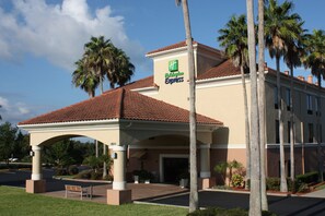 A Holiday Inn Express building with a red-tiled roof, palm trees, and a covered entrance. - Holiday Inn Express Clermont by IHG (Clermont)