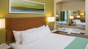 Une chambre d’hôtel avec un grand lit, une salle de bain avec une baignoire et un miroir qui reflète la pièce.