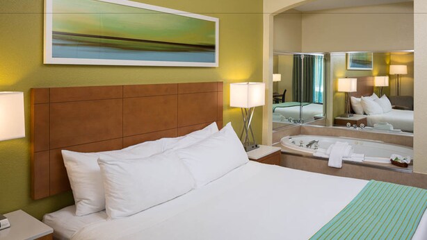 Une chambre d’hôtel avec un grand lit, une salle de bain avec une baignoire et un miroir qui reflète la pièce.