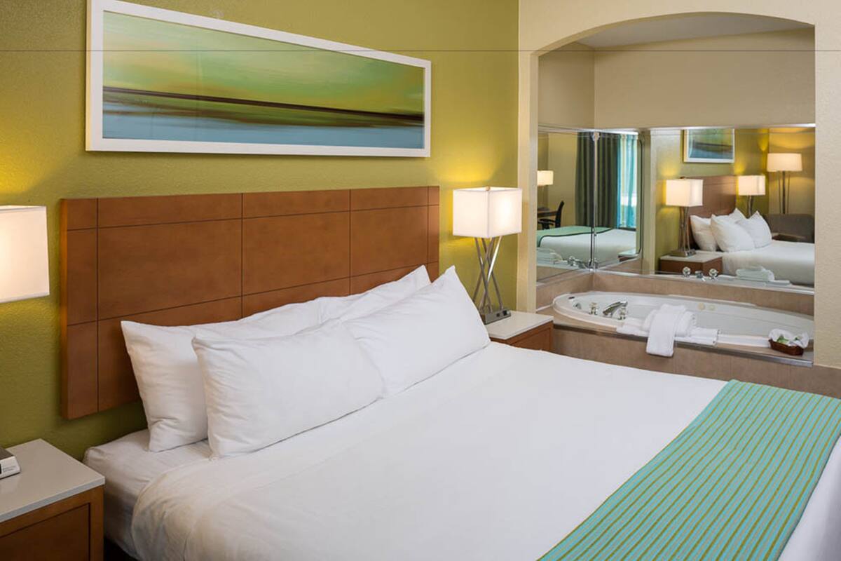 A hotel room with a large bed, a bathroom with a bathtub, and a mirror reflecting the room.