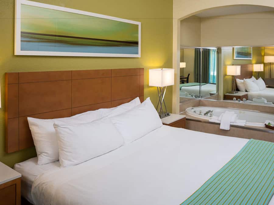 Habitación de hotel con una cama grande, un baño con bañera y un espejo que refleja la habitación.