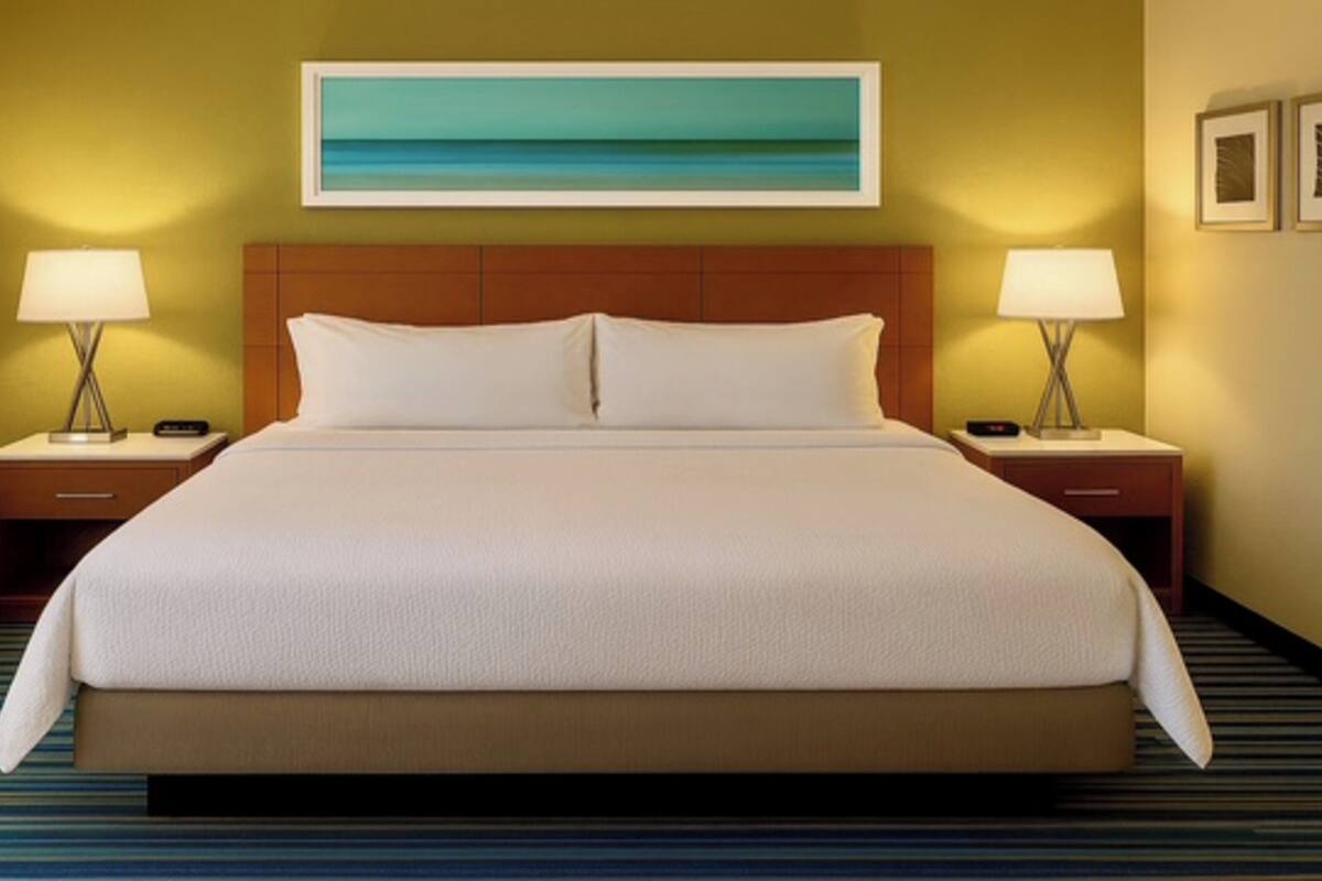 A hotel room with a large bed, two bedside tables with lamps, a headboard, a painting on the wall, and a striped carpet.
