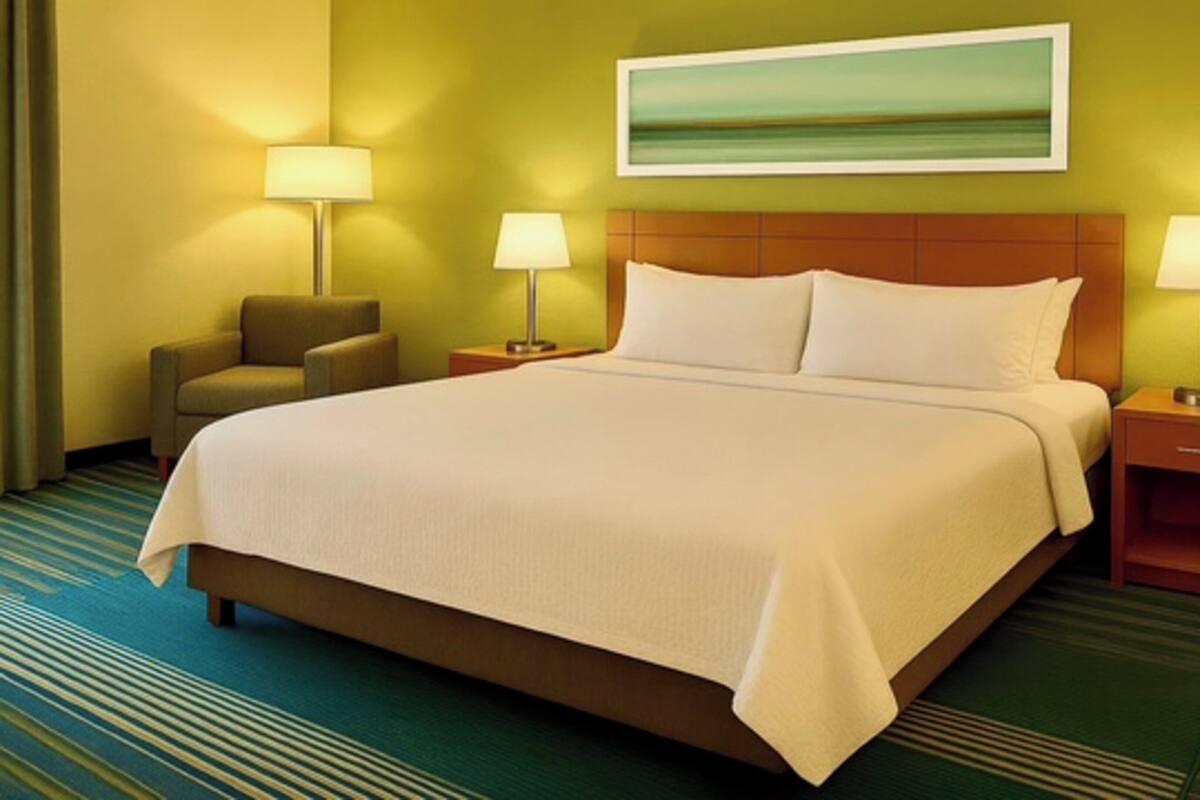 A hotel room with a large bed, two bedside tables with lamps, a chair, and a painting on the wall.