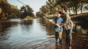 Two people fishing by a calm river surrounded by trees.