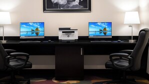 Un espace de travail dans un hôtel équipé de deux écrans d’ordinateur, d’une imprimante et de deux chaises de bureau.