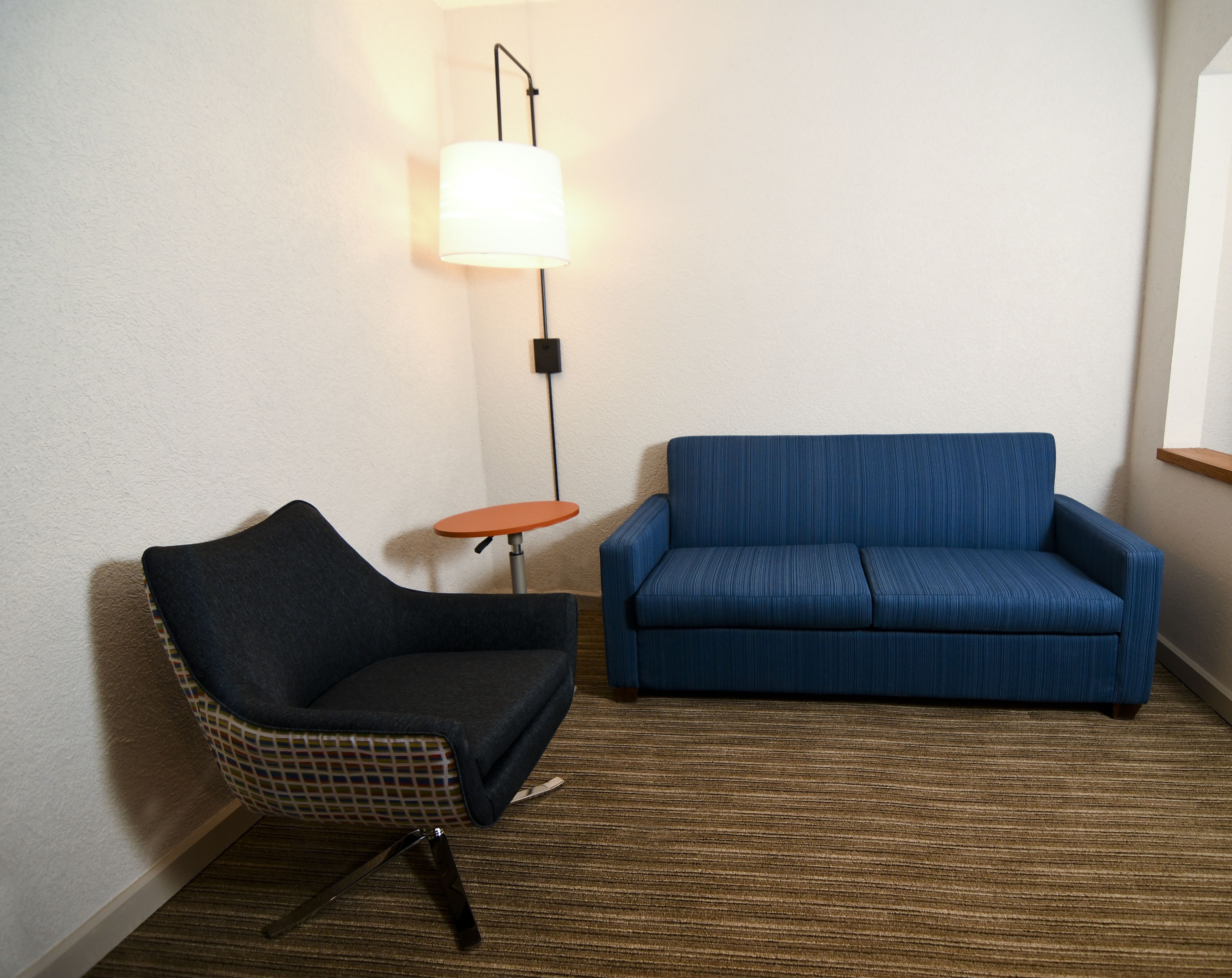 Una habitación con un sofá azul, un sillón estampado y una mesita con una lámpara.