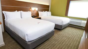 A hotel room with two beds, a wooden headboard, a nightstand, a bedside table, a window with blinds, and a wall-mounted air conditioning unit.