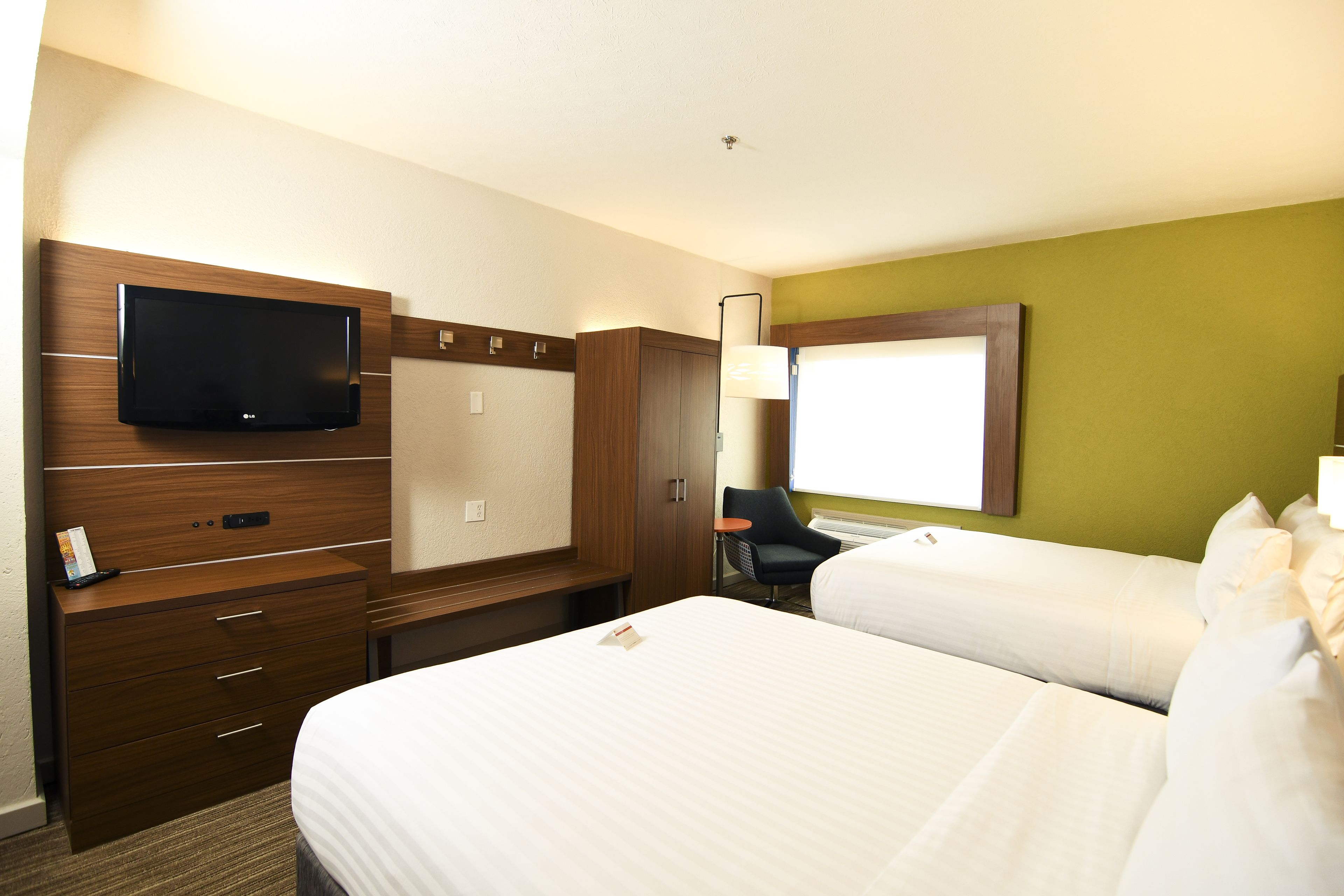 A hotel room with a flat-screen TV, a desk with drawers, a chair, and two beds.
