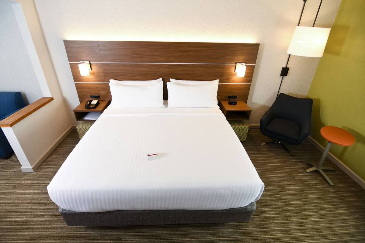 Una habitación de hotel con una cama grande, mesitas de noche, una silla y una pequeña mesa.