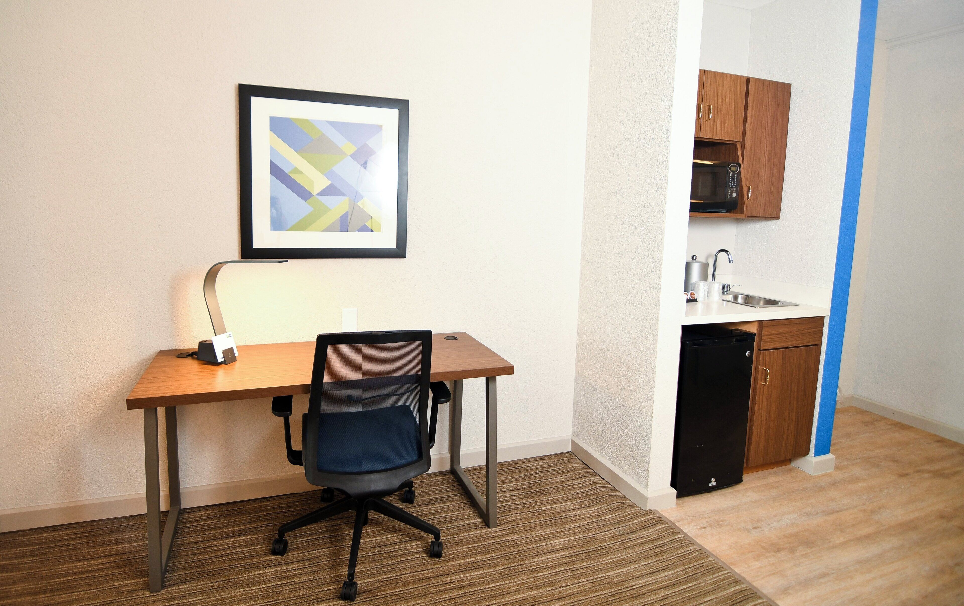 A small office space with a desk, chair, and a framed picture on the wall.