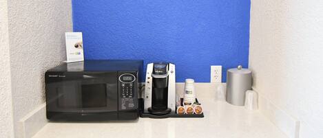Una kitchenette con microondas, cafetera y cápsulas de café sobre una encimera blanca.