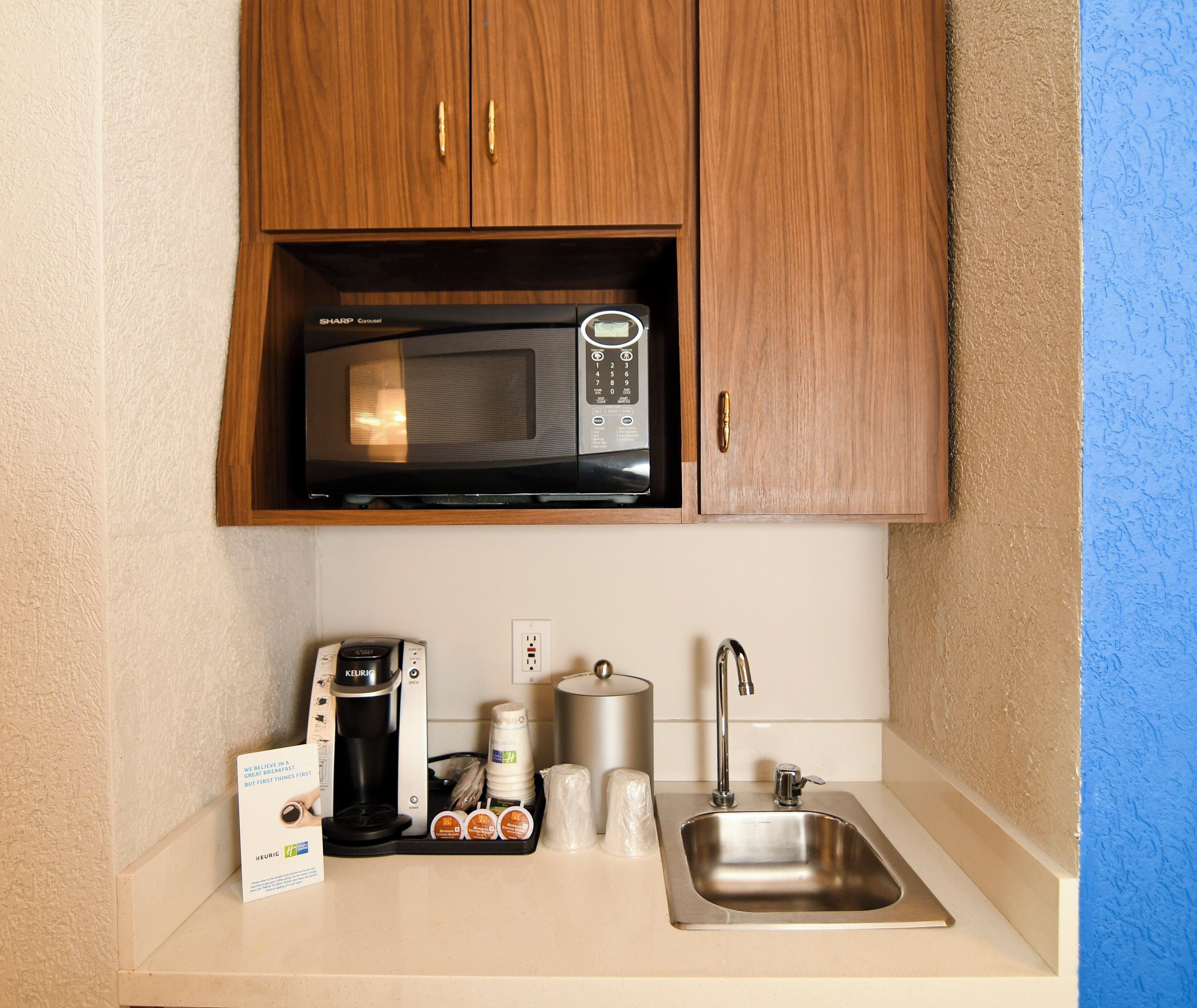 A kitchenette with a microwave, coffee maker, kettle, and a sink.