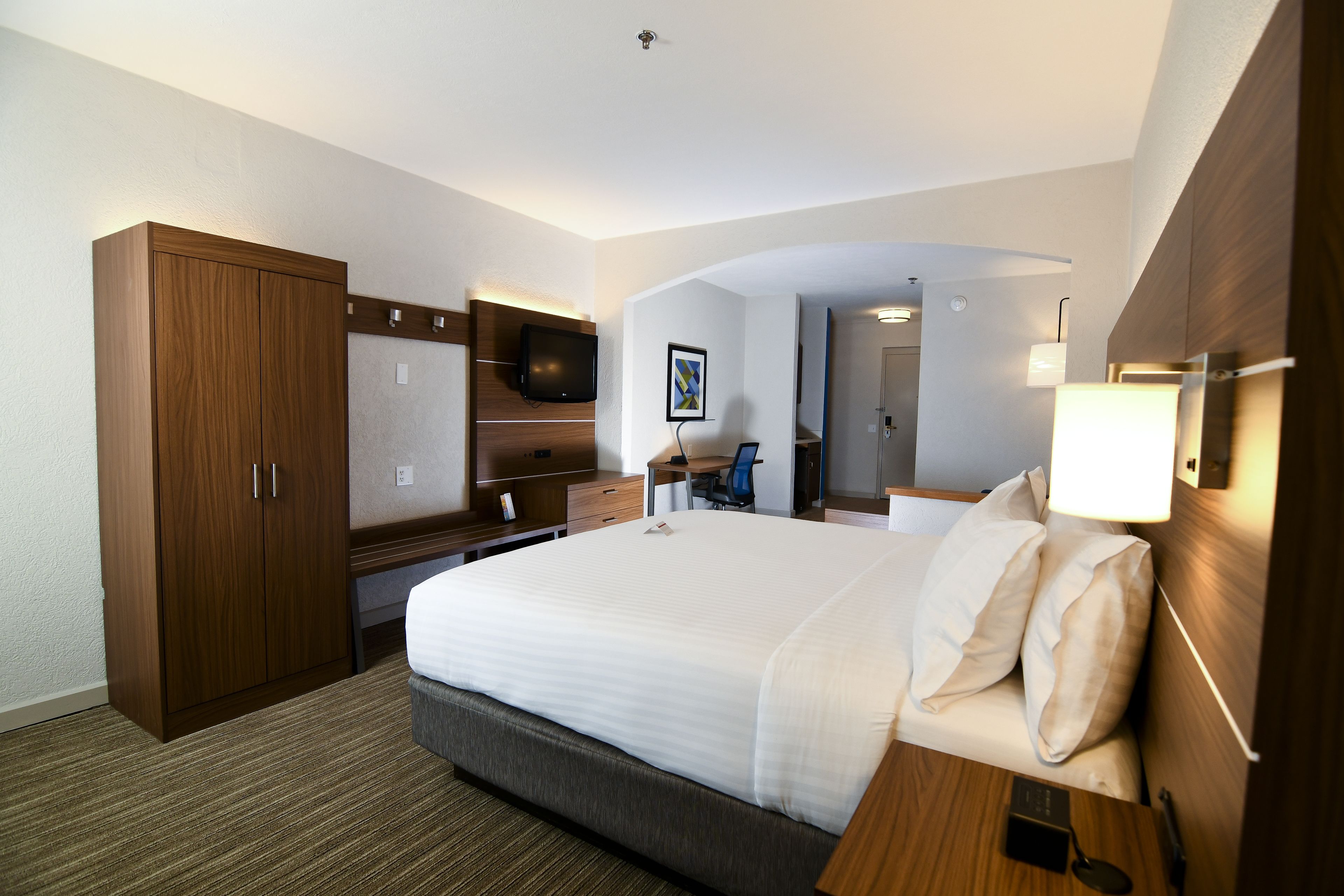 A hotel room with a large bed, wooden wardrobe, desk, chair, and a television.