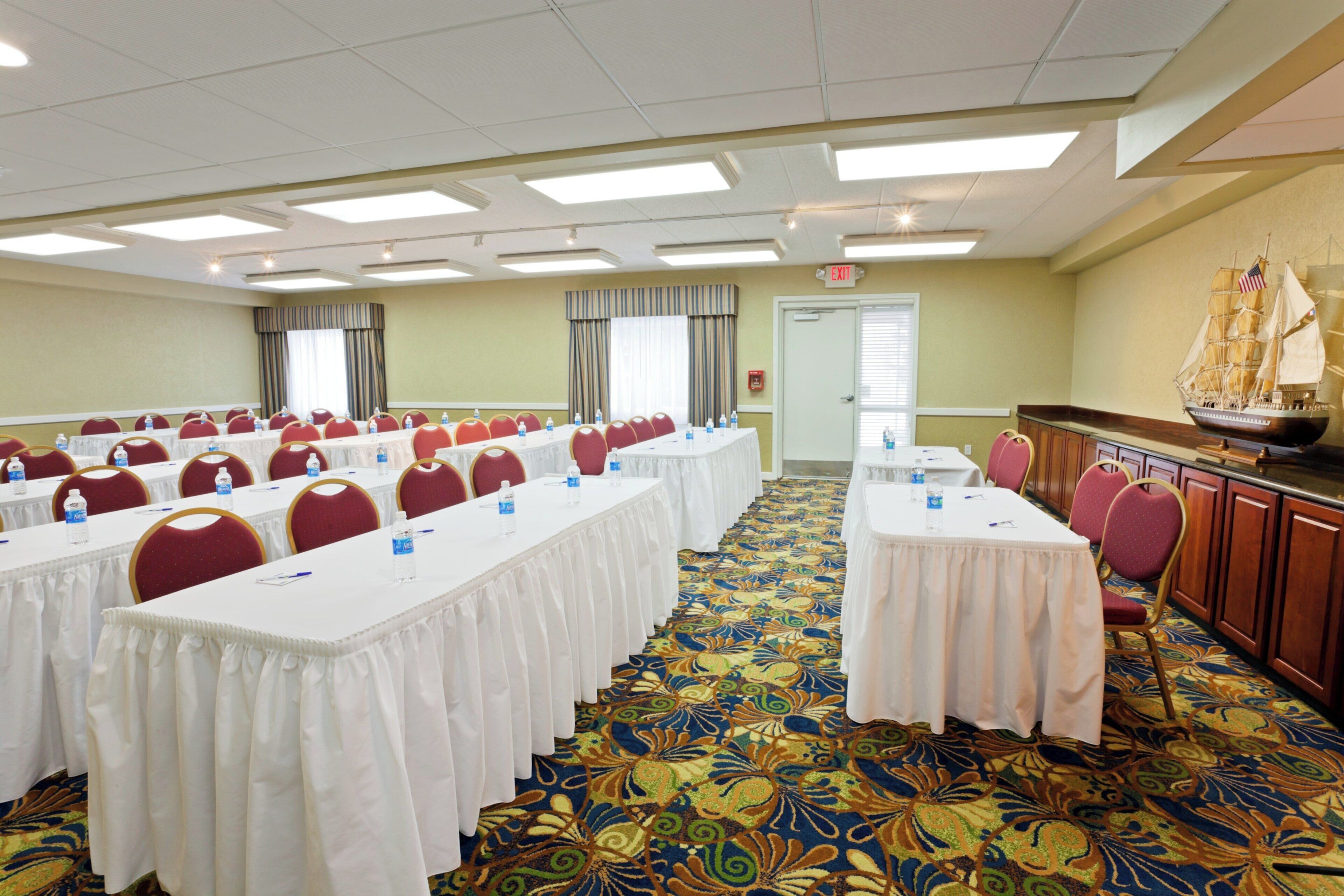A conference room with multiple tables and chairs, a patterned carpet, and a ship model on the wall.