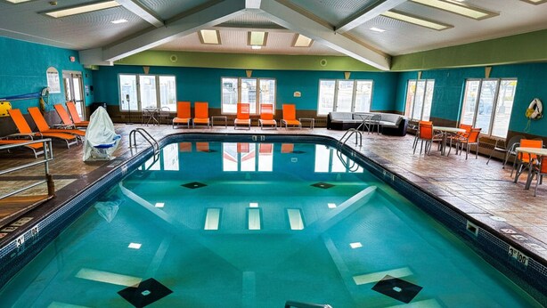 An indoor swimming pool with clear water, surrounded by orange chairs and tables, and large windows allowing natural light. - Holiday Inn Express Hotel & Stes Port Clinton-Catawba Island by IHG (Port Clinton)