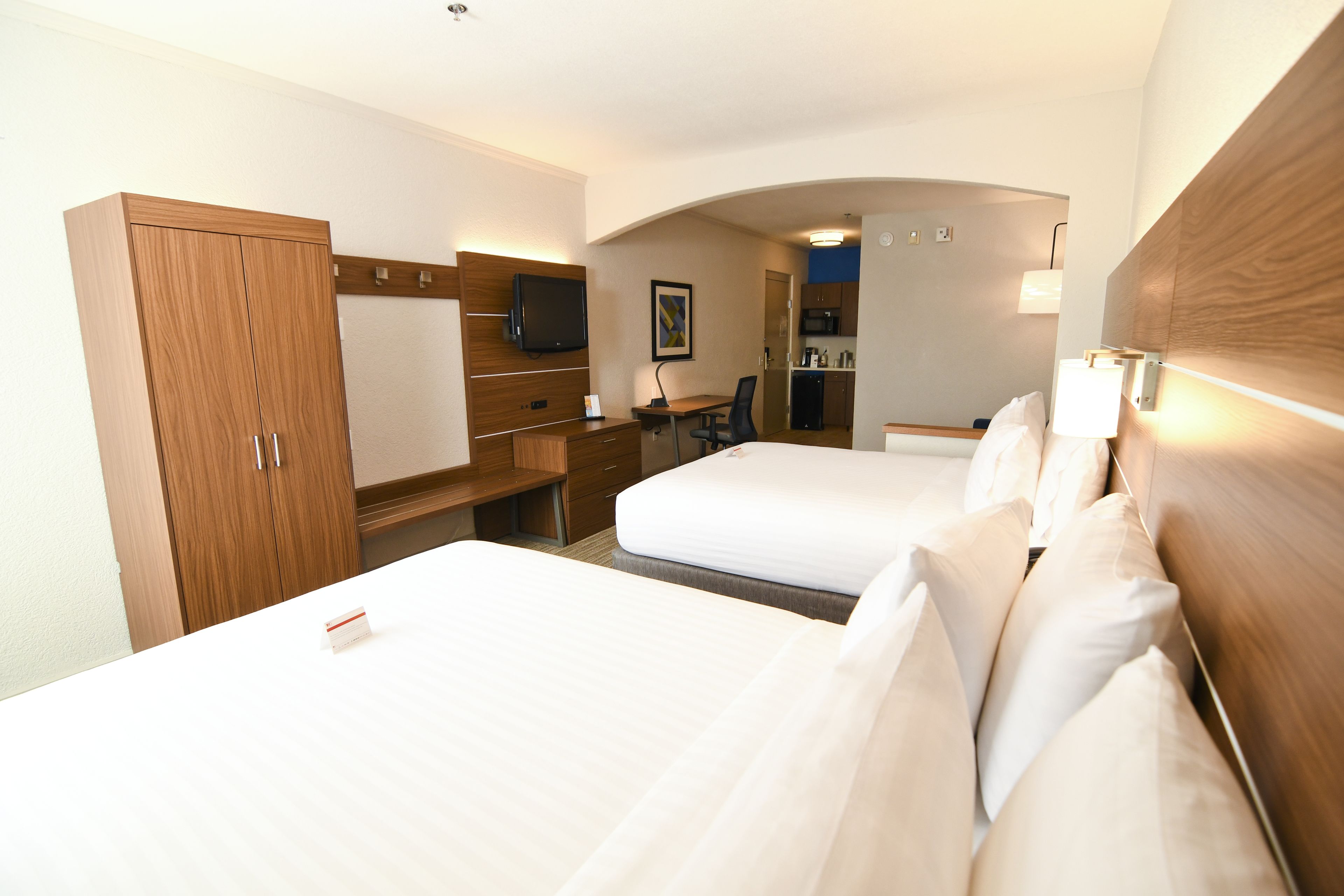 Een hotelkamer met twee bedden, een bureau, een televisie en een kitchenette.