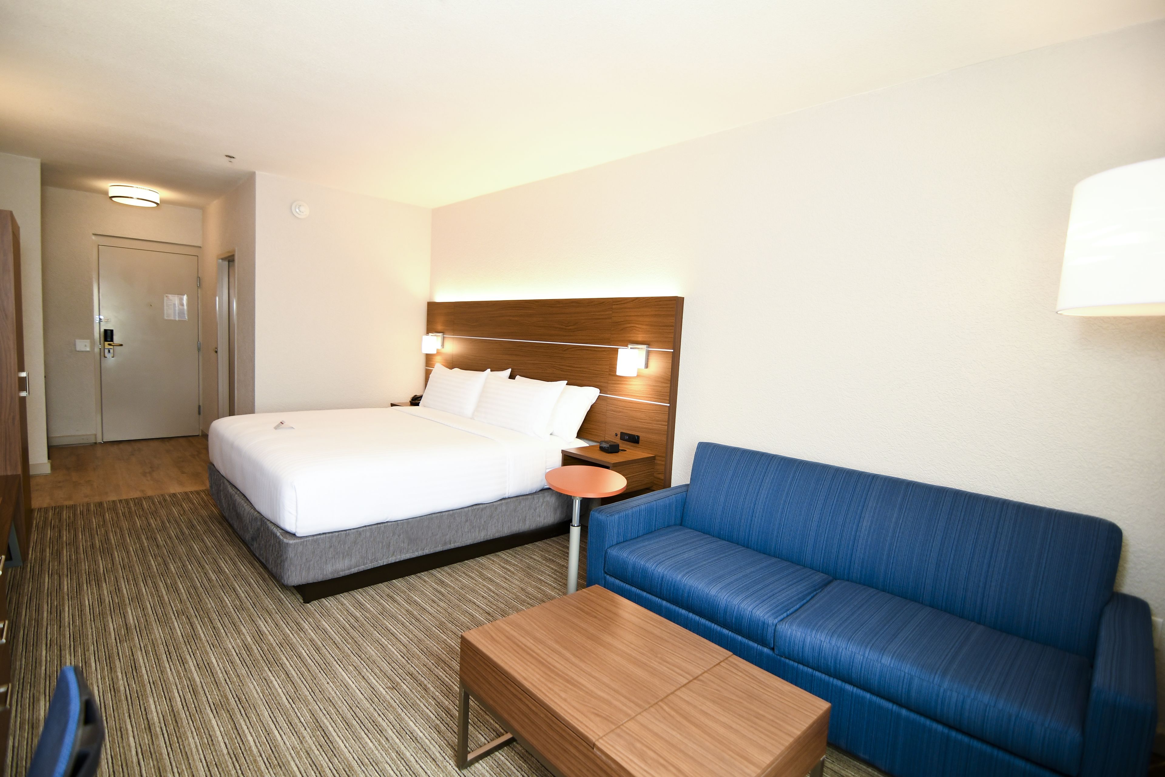 Una habitación de hotel con una cama, un sofá azul, una mesa de madera y una mesita de noche con una lámpara.