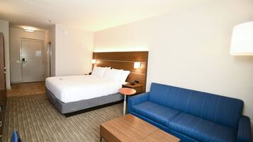 Una habitación de hotel con una cama, un sofá azul, una mesa de madera y una mesita de noche con una lámpara.