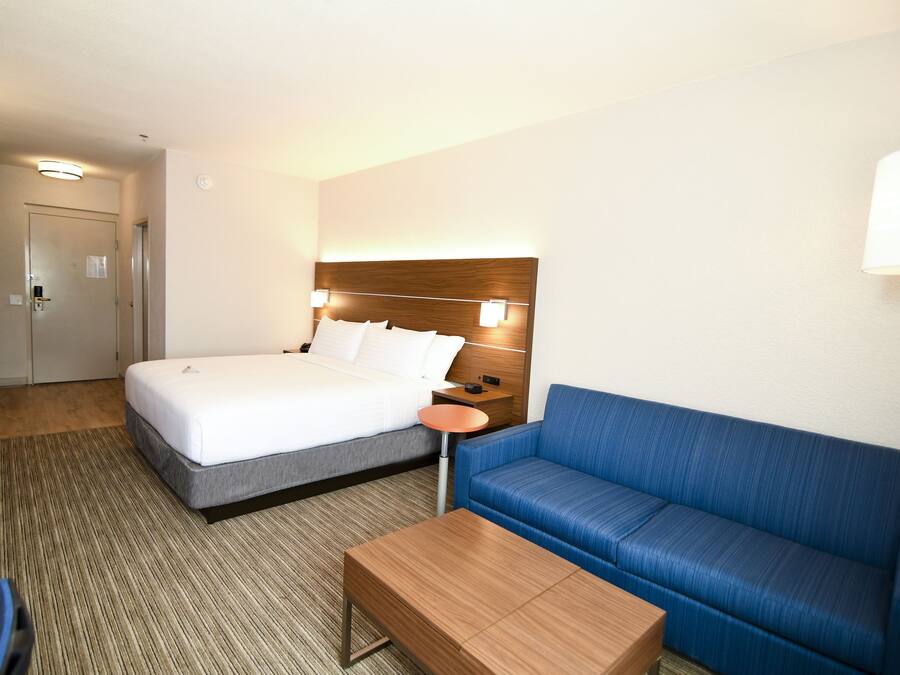 Una habitación de hotel con una cama, un sofá azul, una mesa de madera y una mesita de noche con una lámpara.