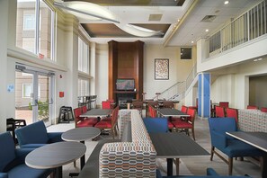 A spacious indoor dining area with high ceilings, multiple tables and chairs, and a central fireplace. - Holiday Inn Express & Suites Port Clinton-Catawba Island by IHG (Port Clinton)