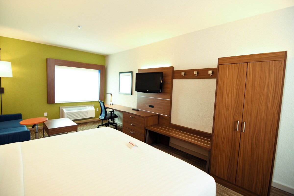 Habitación de hotel con cama, escritorio, silla, televisor y armario.