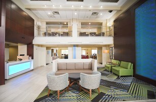 Um hall de hotel com balcão de recepção, área de estar com sofá e duas poltronas, sala de jantar e uma grande tela digital exibindo um padrão azul.