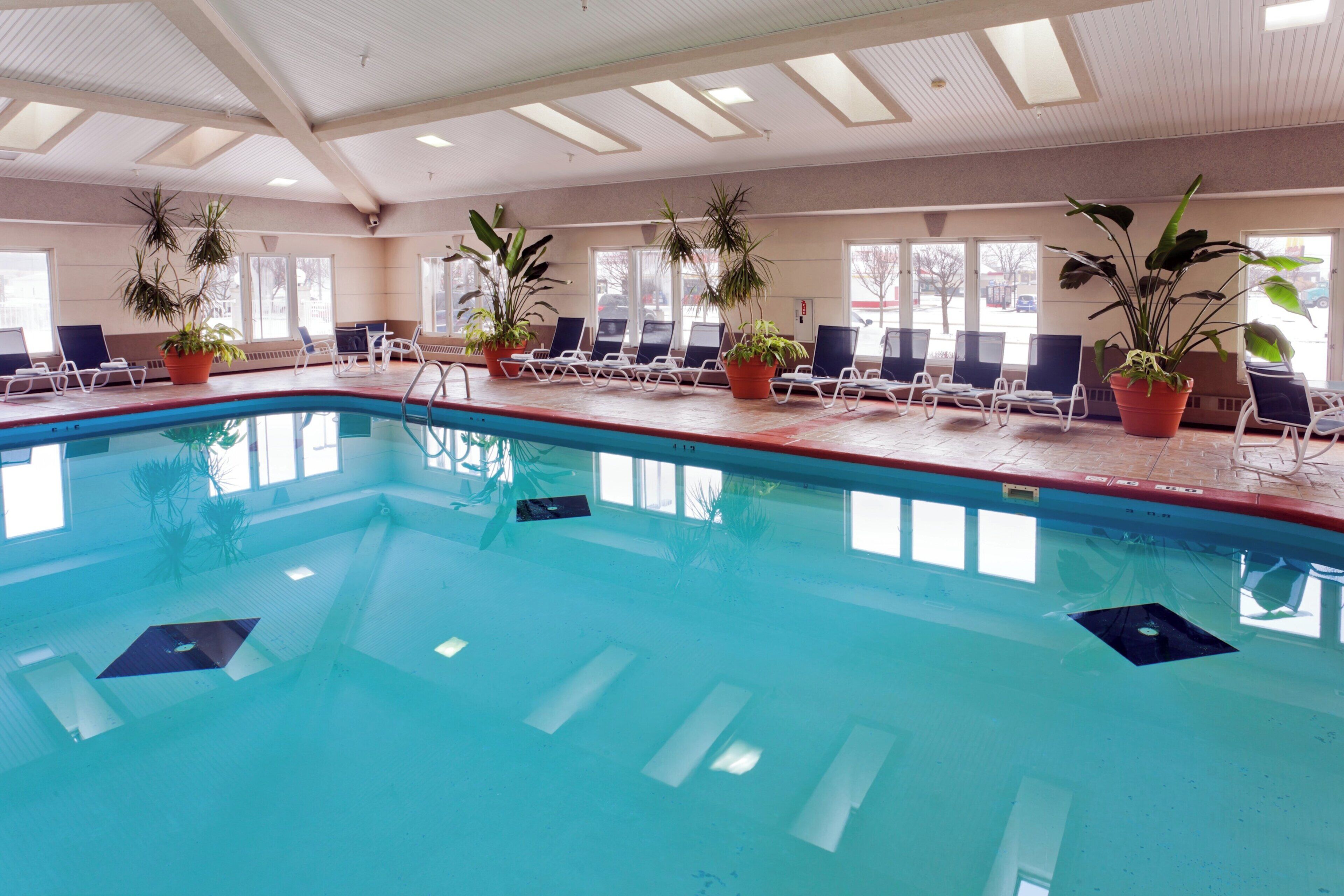An indoor swimming pool with clear water, surrounded by lounge chairs and potted plants.