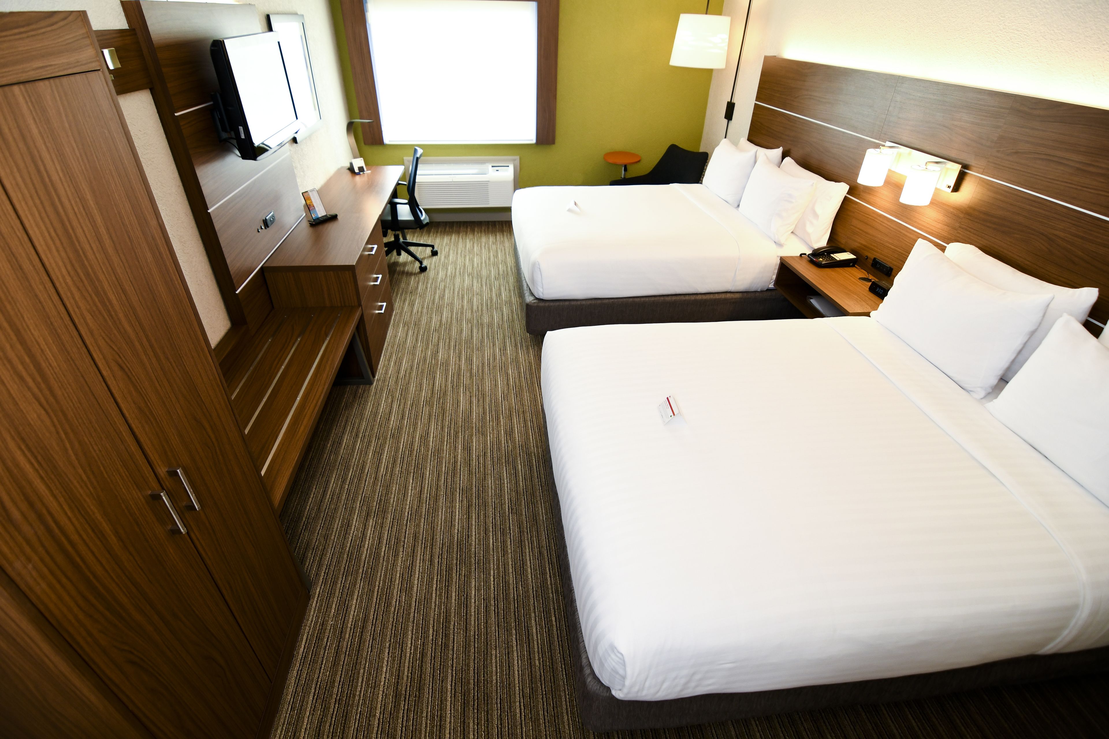 Habitación de hotel con dos camas, un escritorio con silla, televisor y ventana.