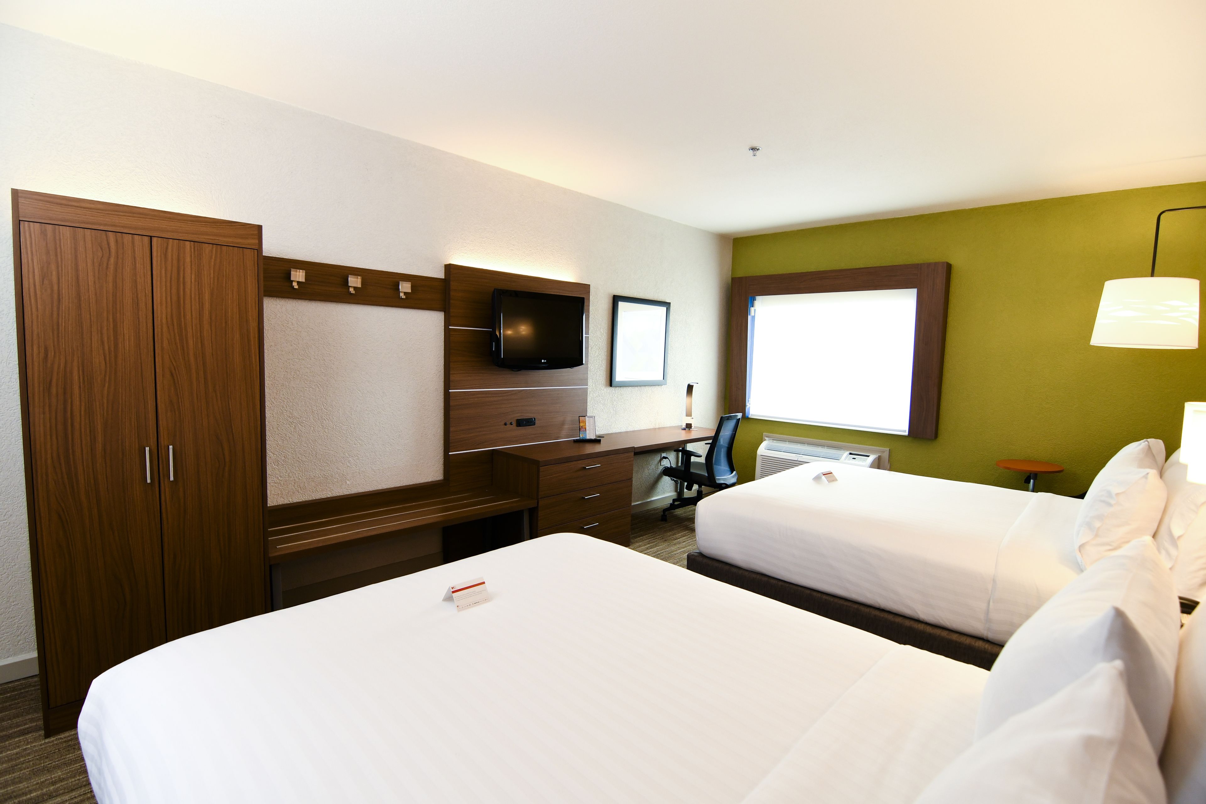 A hotel room with two beds, a desk with a computer, a TV, and a window with blinds.