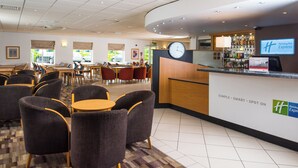 A Holiday Inn Express lobby with a reception desk, seating area with chairs and tables, and a clock. - Holiday Inn Express Gloucester - South by IHG (Gloucester)
