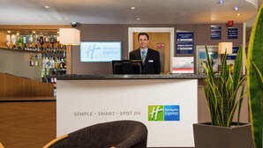 A Holiday Inn Express reception area with a bar, a guest service contact sign, and a general manager notice. - Holiday Inn Express Gloucester - South by IHG (Gloucester)