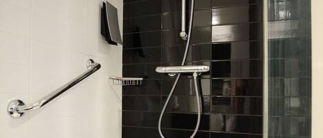A modern bathroom with a black tiled shower wall, a white bathtub, and a handrail.